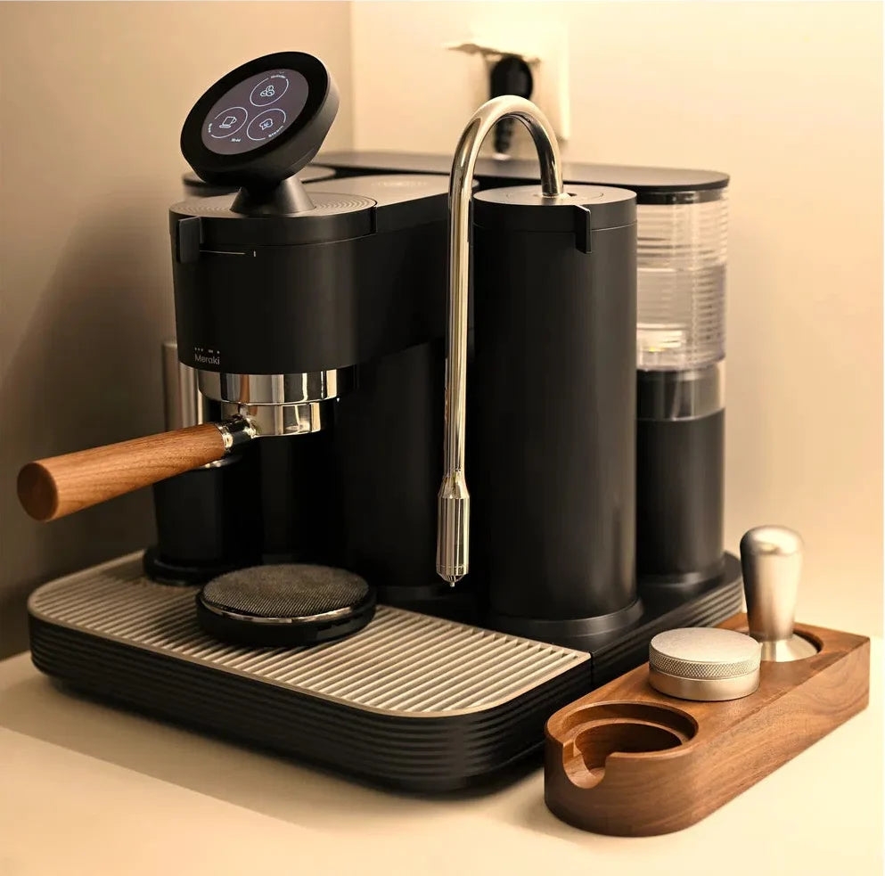 Black Meraki espresso machine with portafilter, steam wand and coffee accessories on a kitchen counter
