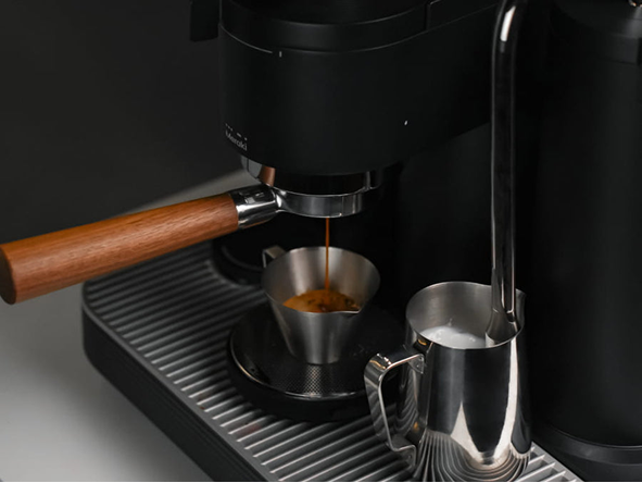 1. Black Meraki espresso machine extracting espresso into a metal cup while steaming milk in a jug