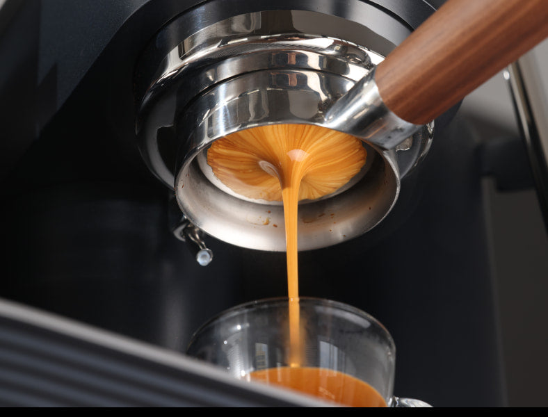 Espresso flowing from a wooden-handled bottomless portafilter into a glass on a black Meraki espresso machine