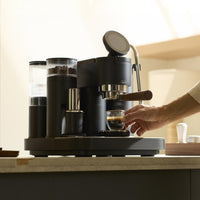 Black Meraki espresso machine with built-in grinder on a kitchen counter, hand picking up a freshly pulled espresso